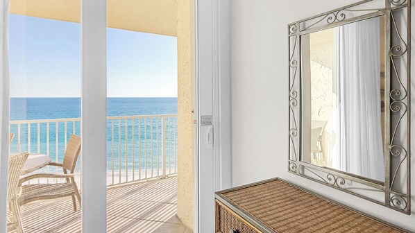Un balcón con vista al océano, una silla de mimbre y un espejo decorativo.