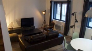 A living room with a sofa, a television, a lamp, and a dining table. - Beautiful renovated house on the waterfront (Treffiagat)
