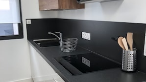 A modern kitchen with a black countertop, wooden cabinets, a stainless steel sink, and a built-in range hood. - Beautiful renovated house on the waterfront (Treffiagat)
