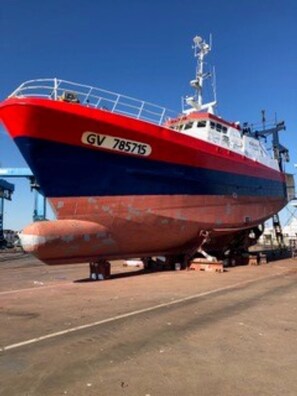 Un grand navire rouge et bleu, portant le numéro d’immatriculation GV 785715, était amarré dans un port.