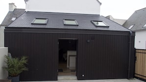 A black metal shed with skylights, a wooden bench, and a potted plant in a residential backyard. - Beautiful renovated house on the waterfront (Treffiagat)