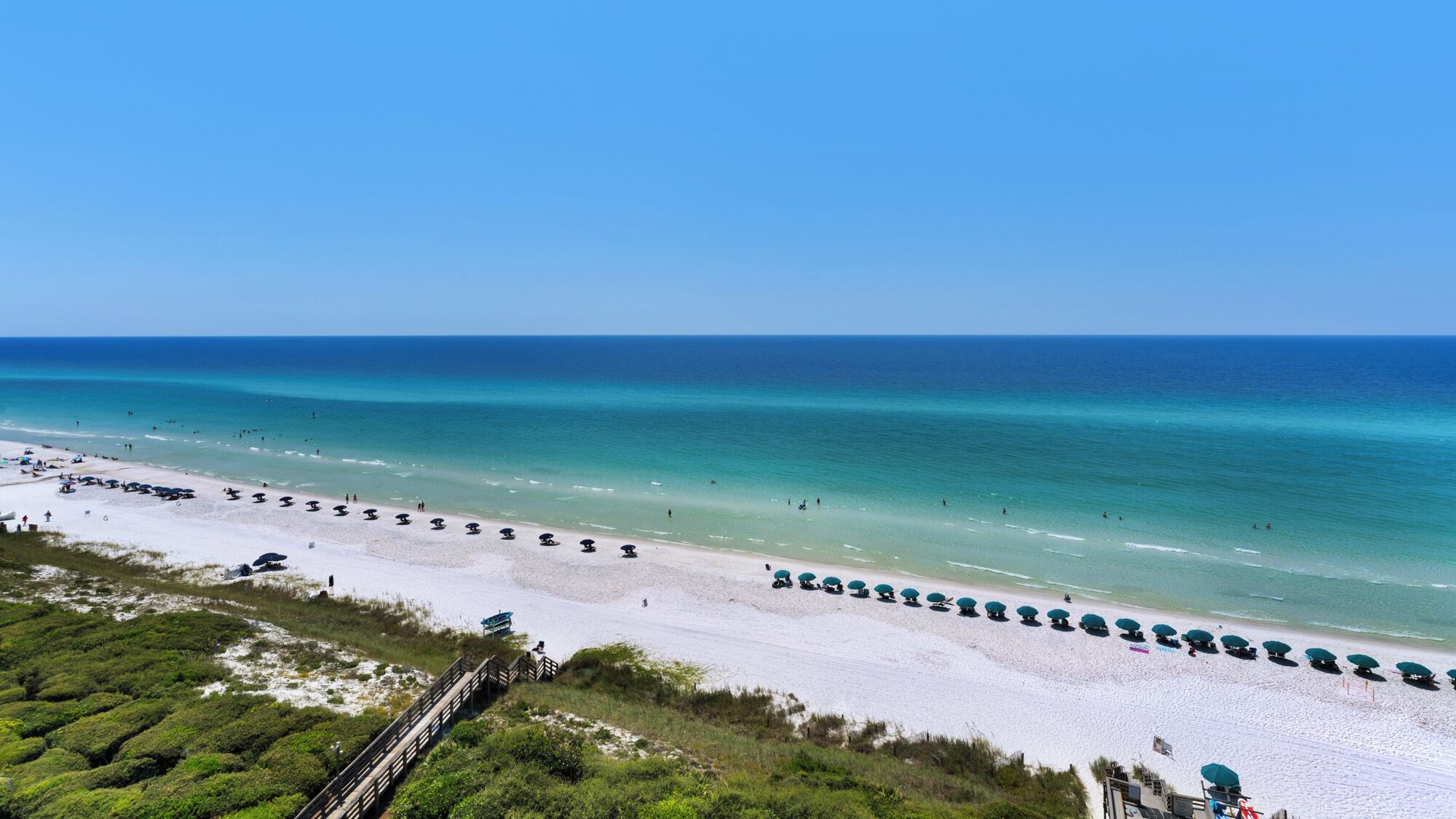 A beach with rows of umbrellas and a wooden walkway leading to the shore.