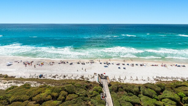 A beach with a wooden walkway leading to the shore, surrounded by dense greenery.