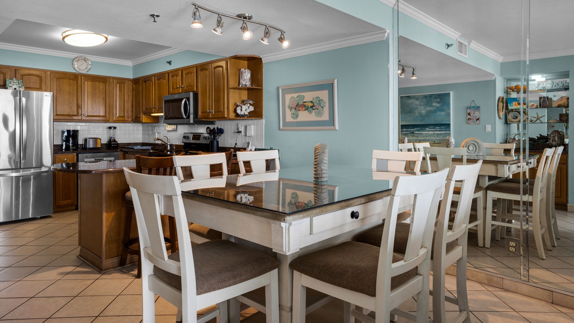 Une cuisine moderne avec des meubles en bois, un réfrigérateur en acier inoxydable et un coin repas comprenant une table en verre et des chaises blanches.