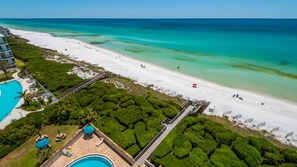Vue aérienne d’un complexe hôtelier en bord de mer, avec une piscine, une plage et une végétation luxuriante.