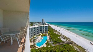 A balcony with a pool and beach view, a modern building with multiple floors, and a clear blue sky. - Private Beach Access, Heated Pool, Beach Chairs + Free Attraction Tickets! (Santa Rosa Beach)