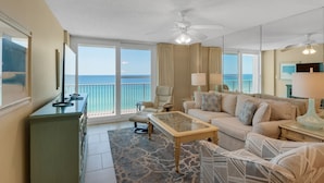 A spacious living room with a large window offering a view of the ocean, a ceiling fan, and a sofa with patterned cushions. - Private Beach Access, Heated Pool, Beach Chairs + Free Attraction Tickets! (Santa Rosa Beach)