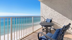 A balcony with a white railing, a round metal table, two chairs with blue cushions, and a view of the ocean. - Gulf Front, Private Beach w/ Beach Setup, Pool + Free Attraction Tickets! (Santa Rosa Beach)