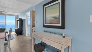 A room with a view of the ocean, a framed painting, a welcome sign, and a wooden table. - Gulf Front, Private Beach w/ Beach Setup, Pool + Free Attraction Tickets! (Santa Rosa Beach)