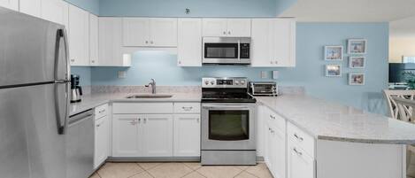 A modern kitchen with white cabinets, stainless steel appliances, a microwave, a stove, and a sink.