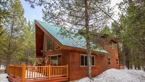 A cabin with a wooden exterior, a green roof, and a deck.