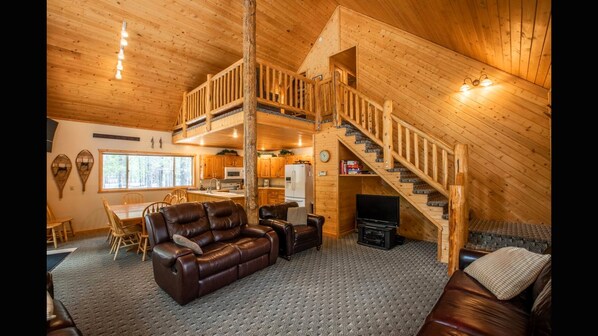 Ein Blockhaus-Innenraum mit Wohnzimmer, Essbereich, Küche und einer Treppe.