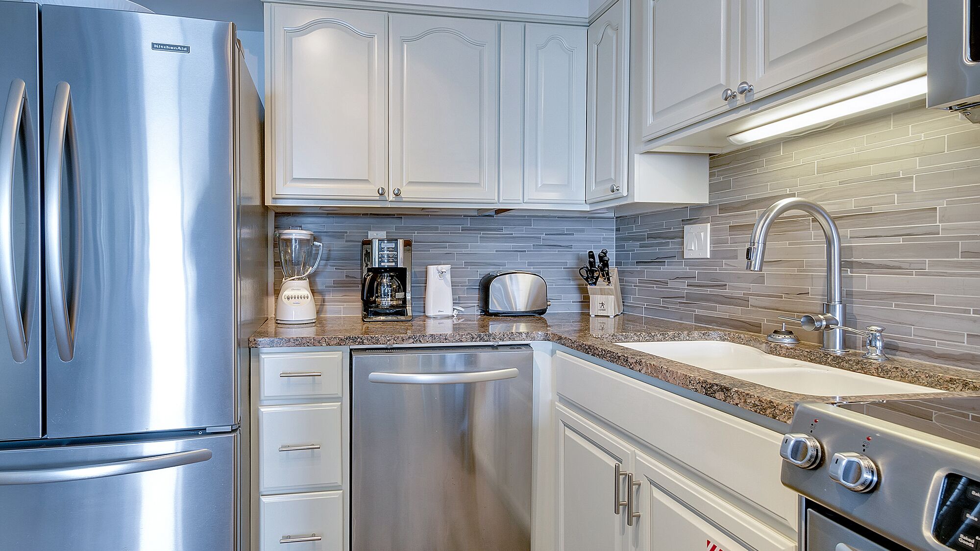 A modern kitchen with stainless steel appliances, white cabinetry, a granite countertop, and a tiled backsplash.