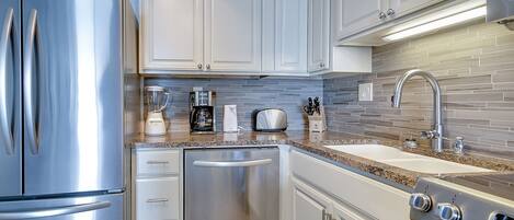 A modern kitchen with stainless steel appliances, white cabinetry, a granite countertop, and a tiled backsplash.