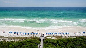 A beach with a wooden walkway leading to the shore, lined with blue umbrellas and beach chairs.