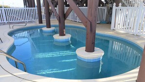 Una piscina con un solarium bianco e un recinto in legno bianco sullo sfondo.