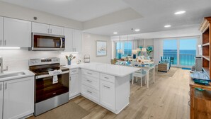 A modern kitchen with white cabinetry, stainless steel appliances, and a large island. There is a dining area with a view of the ocean. - Gulf-Front w/ Private Beach Access + Free Beach Setup & Attraction Tickets! (Santa Rosa Beach)