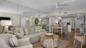 A spacious living room with a sofa, coffee table, and dining area. - Modern Gulf Front Condo, Private Beach Access, Beach Service + Free Tickets! (Santa Rosa Beach)