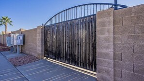 A gated entrance with a metal gate, a brick wall, and a paved pathway. - Quiet Retreat w/ AC | Chelsea Park Casita (Mesa)