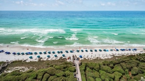 A beach with rows of umbrellas and a wooden walkway leading to the water.