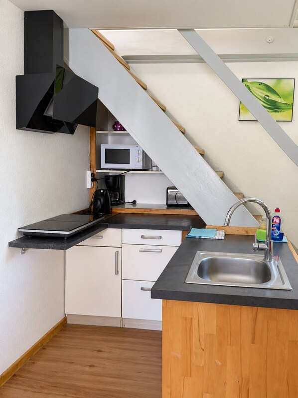 Una cocina compacta con microondas integrado, cafetera y lavabo.