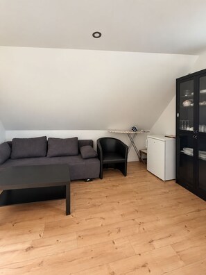 Uma sala de estar moderna com um sofá, uma poltrona, uma mesinha, um armário e um eletrodoméstico branco.