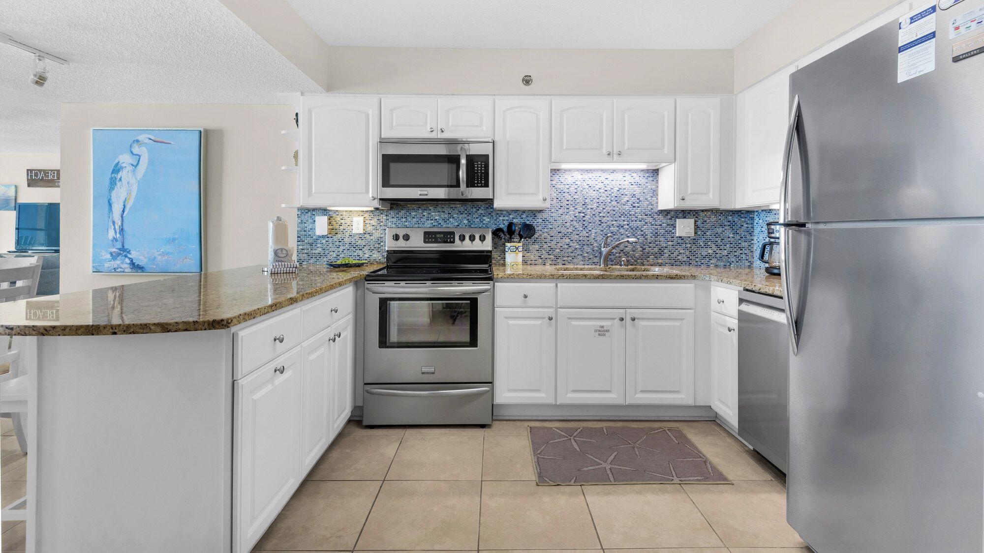 A modern kitchen with white cabinets, stainless steel appliances, and a blue mosaic backsplash.