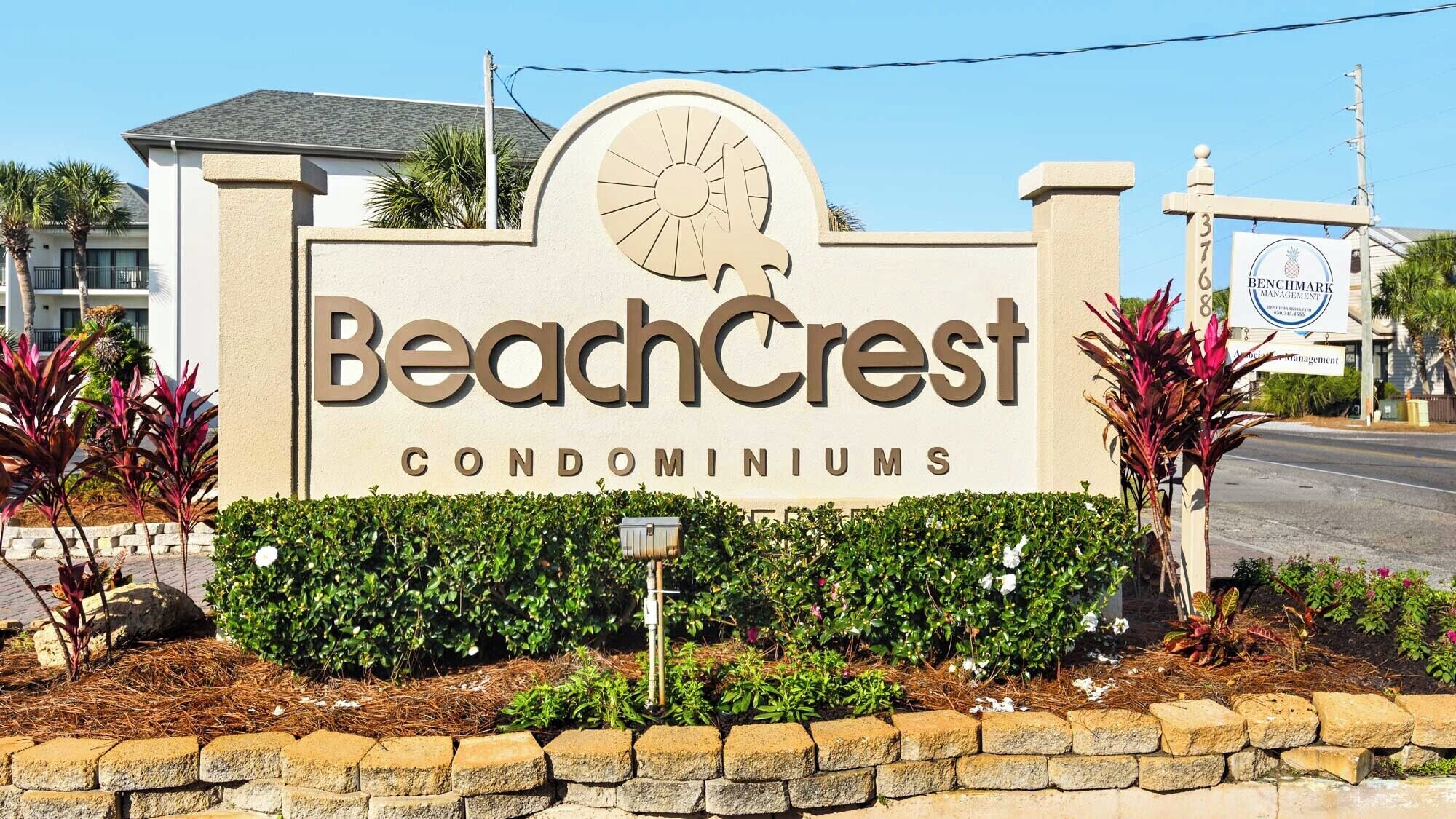 A sign for BeachCrest Condominiums with a sun and palm tree design.