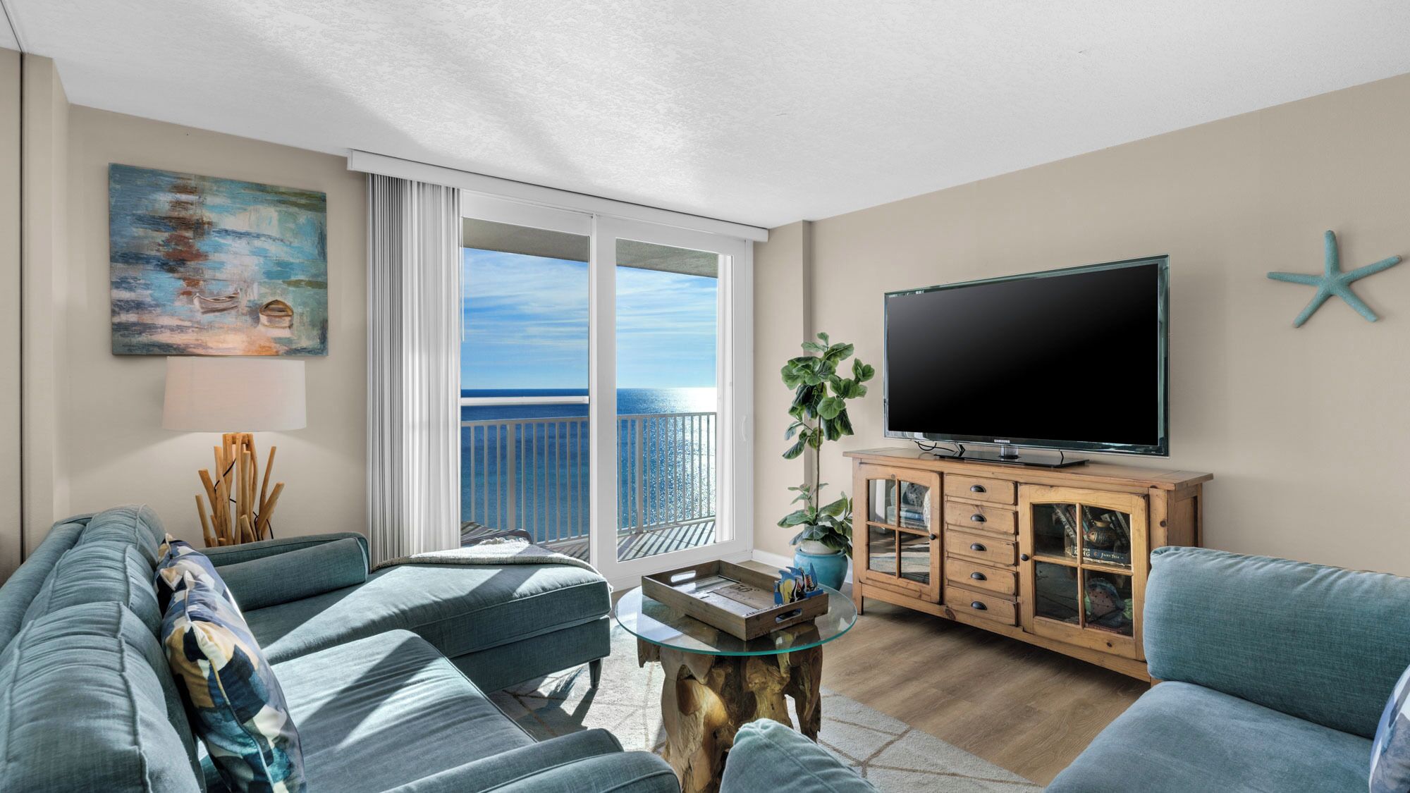 Een woonkamer met een bank, een salontafel, een televisie en een balkon met uitzicht op zee.