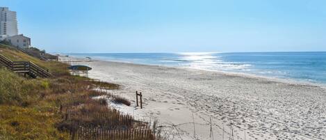 A beach with a wooden staircase leading to a building, a sandy shore, and the ocean.