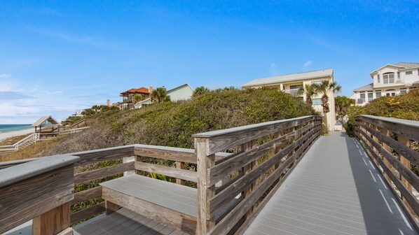 A wooden boardwalk leading to beachfront properties with a beach and ocean in the background.