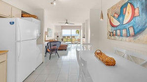 A modern kitchen with white appliances, a dining area with a white table, and a large abstract painting on the wall. - Dog Friendly Gulf-Front Condo in Seagrove Beach, Sleeps 6 + Free Tickets! (Santa Rosa Beach)