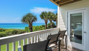 A balcony with two chairs, a door with a glass panel, and a view of the ocean and palm trees.