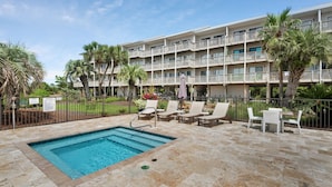 A hotel with a swimming pool, lounge chairs, and palm trees.
