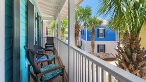 A porch with wicker chairs and a view of a blue house and palm trees. - Charming Patio Home, Community Pool and a Brand New Beach Access Point! (Santa Rosa Beach)