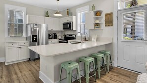 A modern kitchen with white cabinetry, stainless steel appliances, and a central island with bar stools. - Charming Patio Home, Community Pool and a Brand New Beach Access Point! (Santa Rosa Beach)