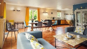 A spacious living area with a sofa, a dining table, and chairs. There is a kitchen area with a refrigerator and a sink.