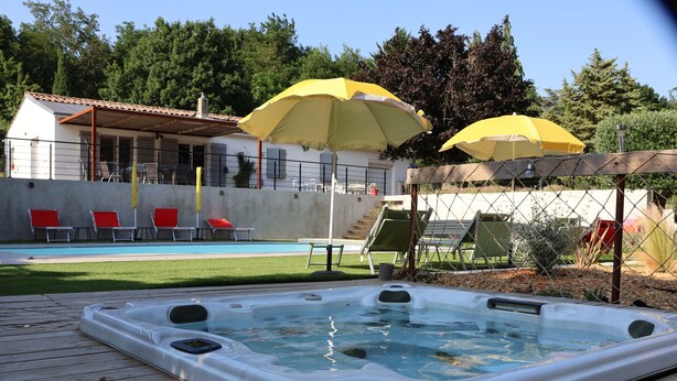 A hot tub on a wooden deck, a swimming pool, and red lounge chairs.