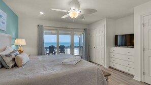 Enjoy a restful night's sleep in this spacious bedroom with a large bed, ceiling fan, and TV, plus a balcony with ocean views.