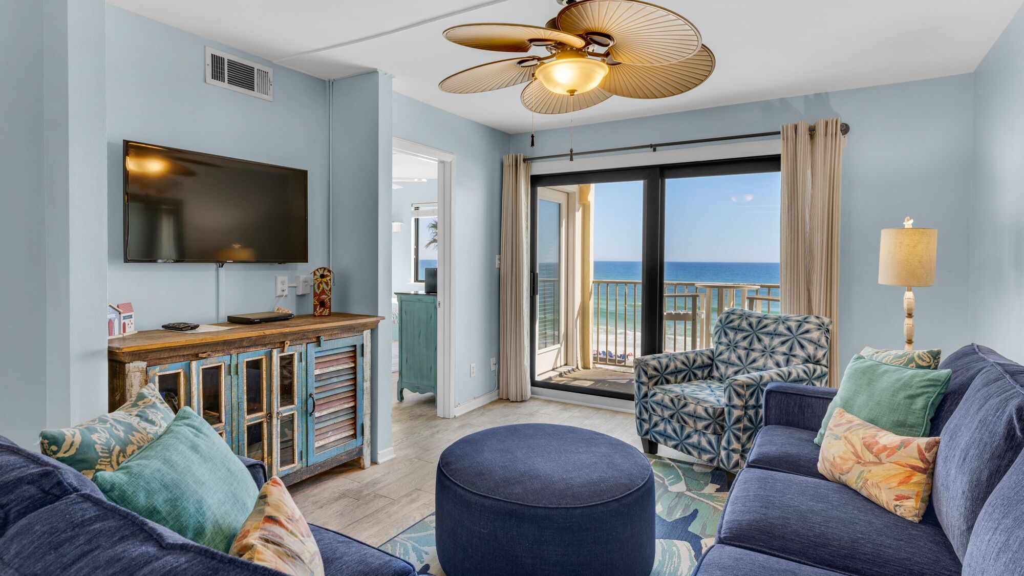 A modern living room with a large TV, a ceiling fan, and a view of the ocean.