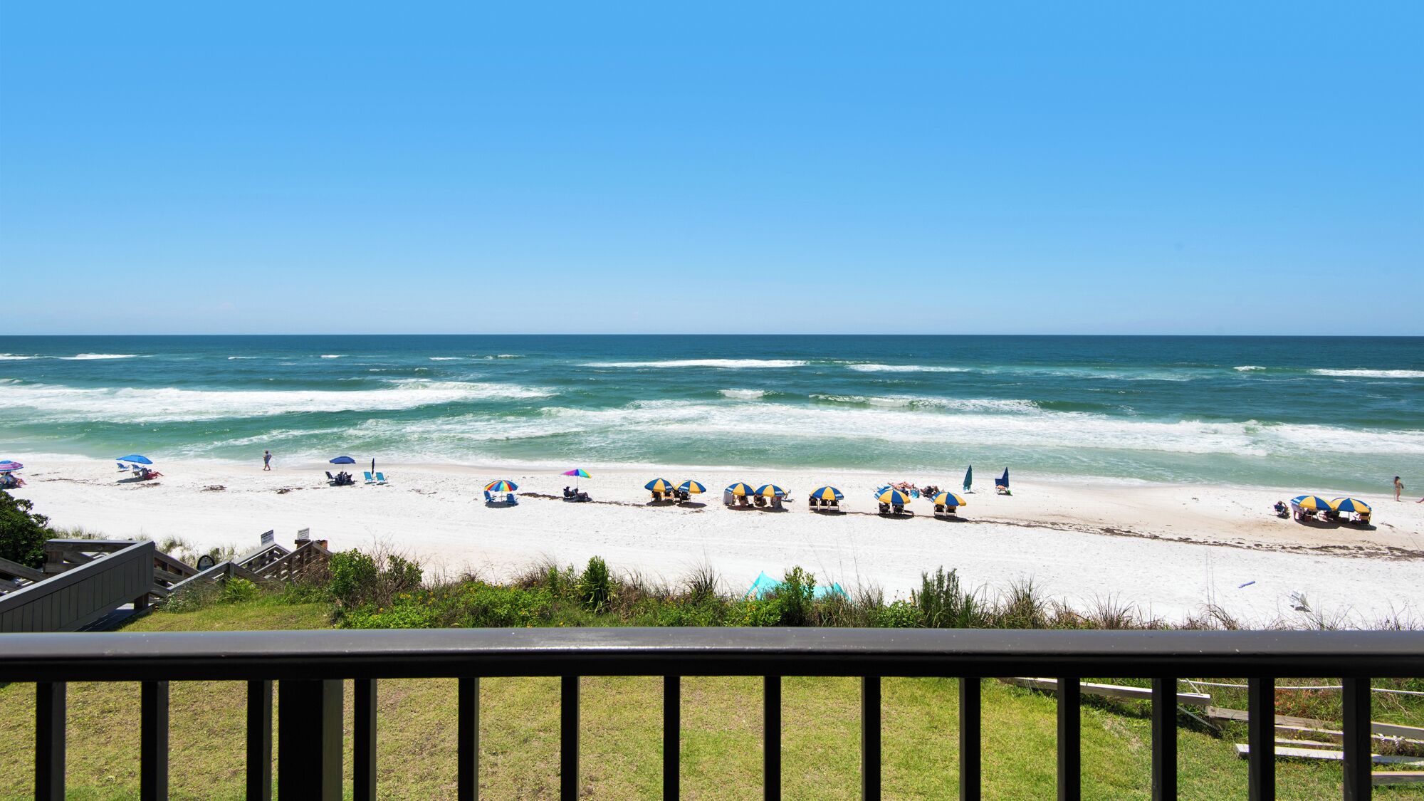 A beach with umbrellas and people, a clear sky, and ocean waves.