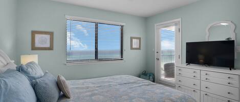 A bedroom with a bed, a dresser, a television, and two windows with blinds.