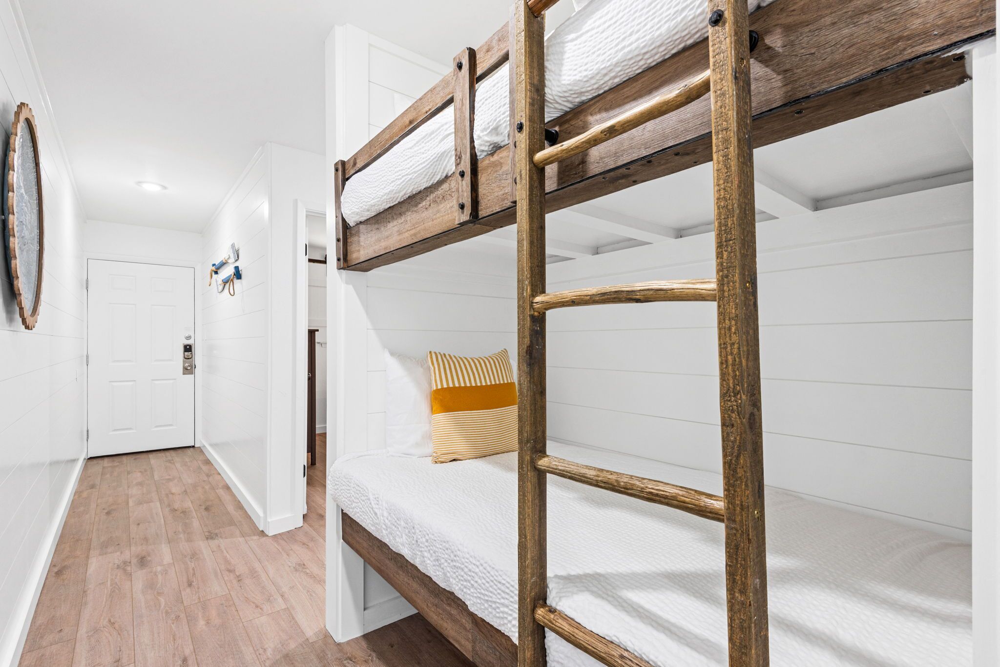 A bunk bed with a ladder, a wooden floor, and a white door in the background.