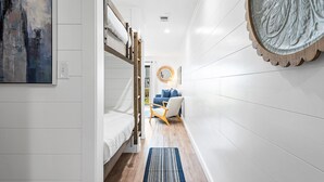 A narrow hallway with a bunk bed, a blue chair, a round mirror, and a blue rug. - 1st Floor, Gulf Side in Seagrove,  Sleeps 6 + Free Attraction Tickets! (Santa Rosa Beach)