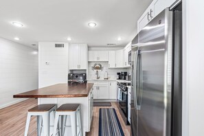 Une cuisine moderne avec des meubles blancs, un réfrigérateur en acier inoxydable, un îlot central en bois avec des tabourets, et un four encastré.