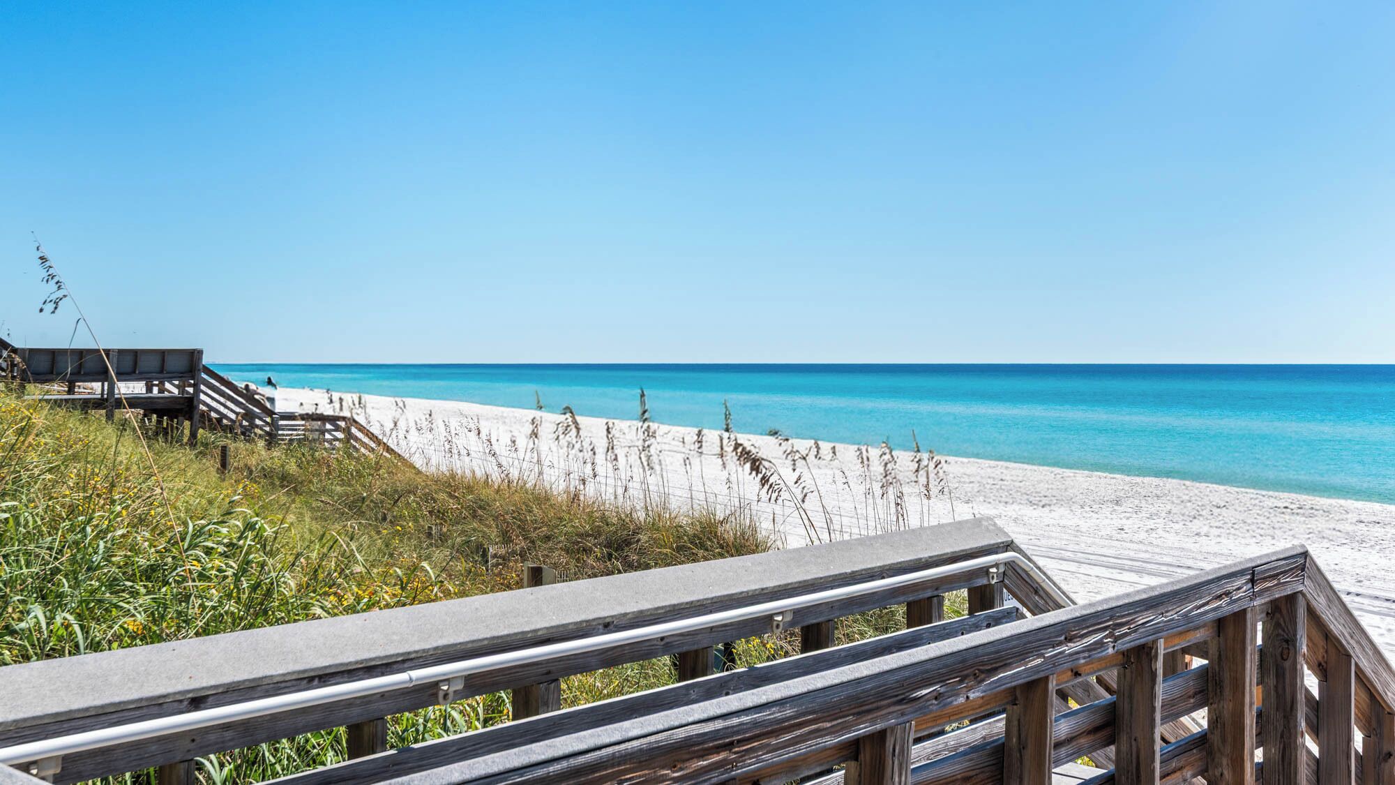 A wooden boardwalk leading to a sandy beach with clear blue water.