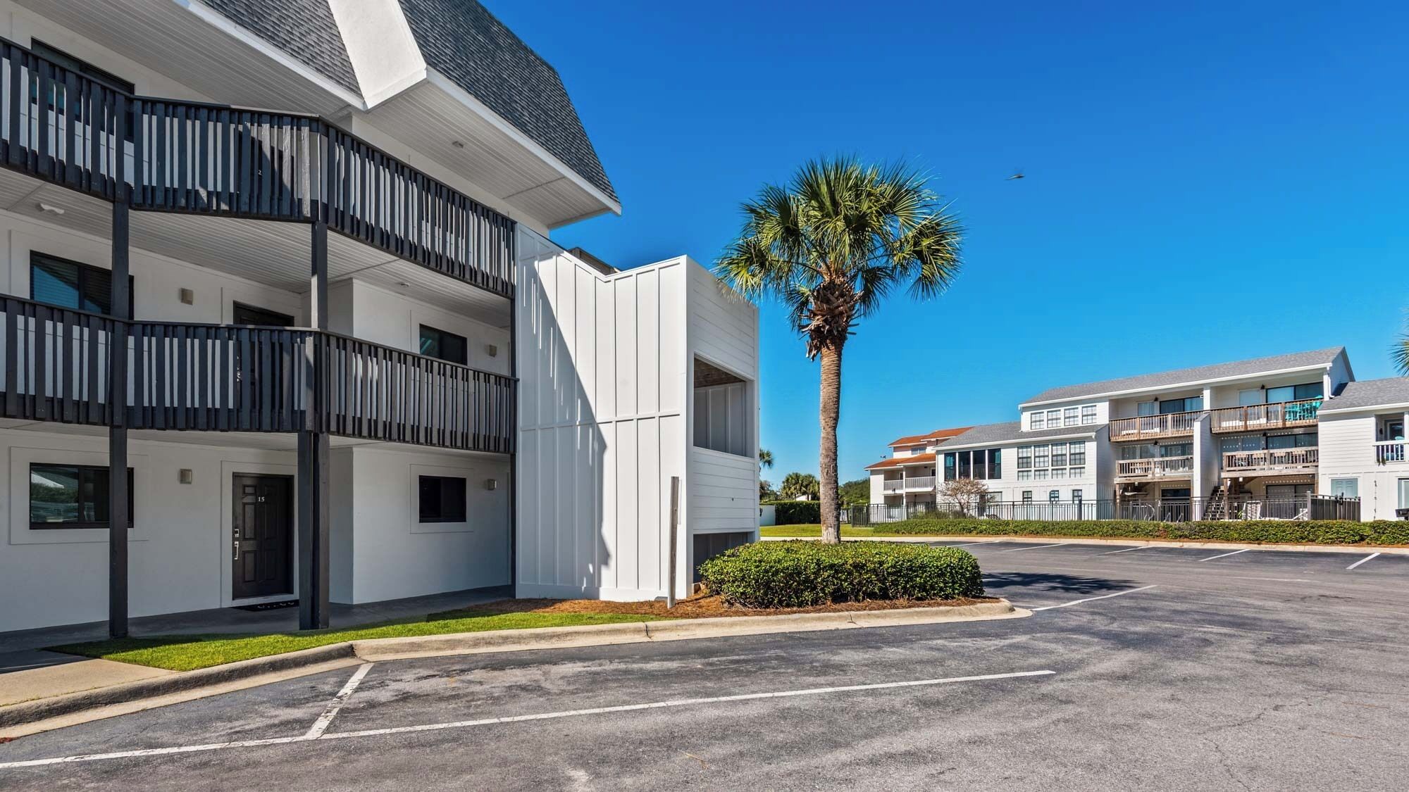 A modern multi-story hotel with balconies, a parking lot, and a palm tree.