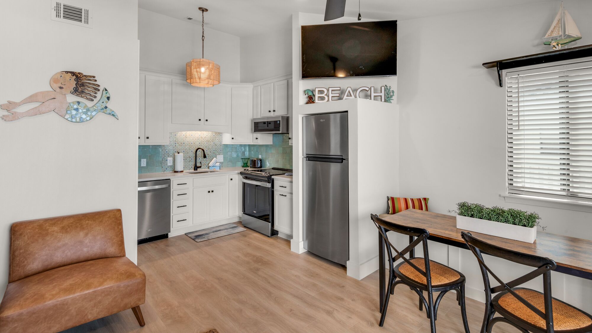 A modern kitchen with white cabinets, stainless steel appliances, and a wooden dining table with two chairs.