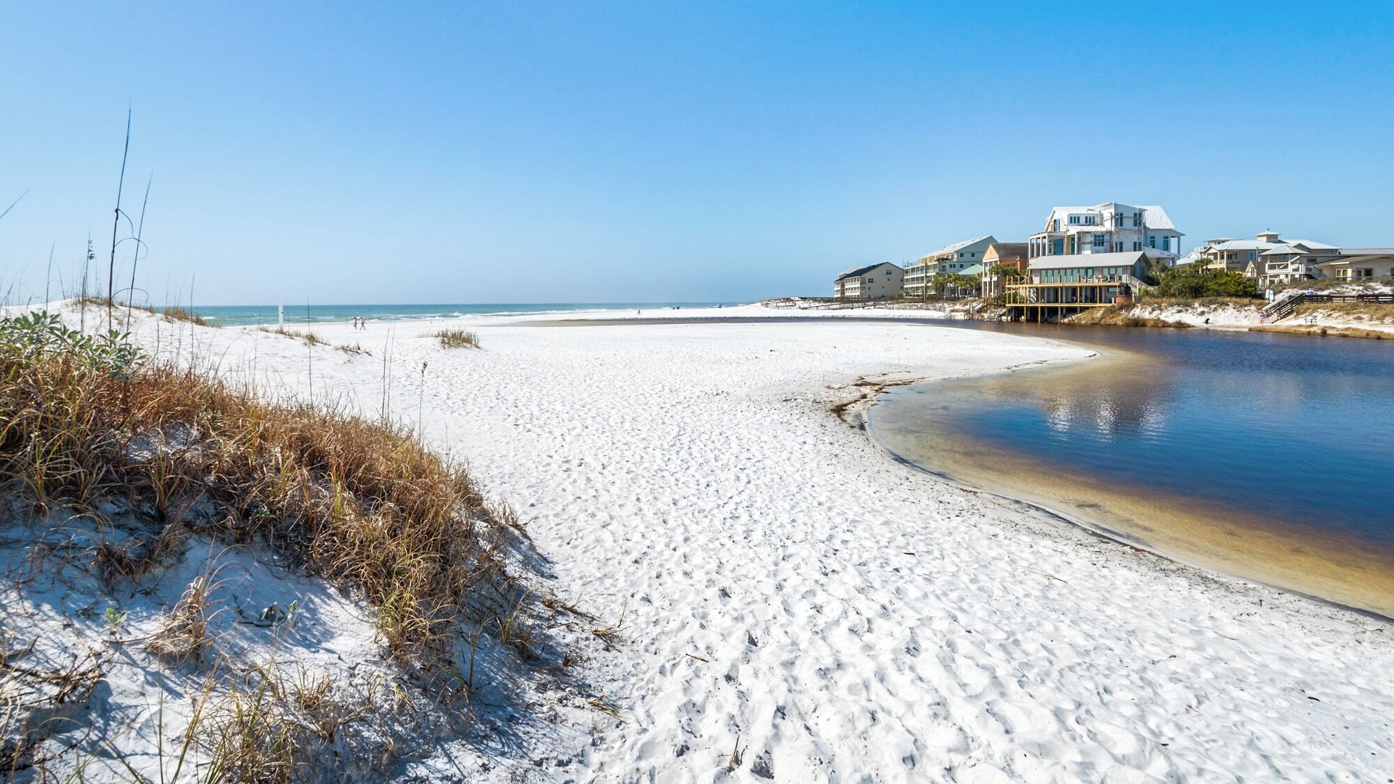 A beach with white sand, a calm water body, and beachfront properties.