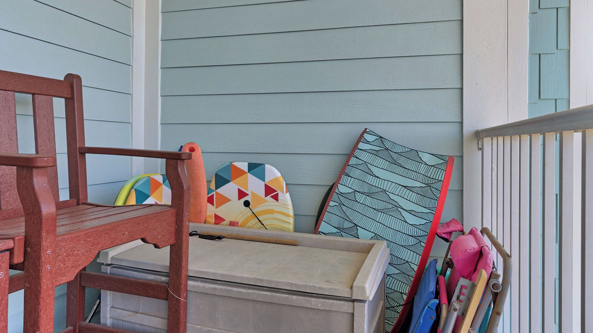 Une chaise en bois et une boîte de rangement sur un porche dont le mur extérieur est recouvert de lambris bleu clair.